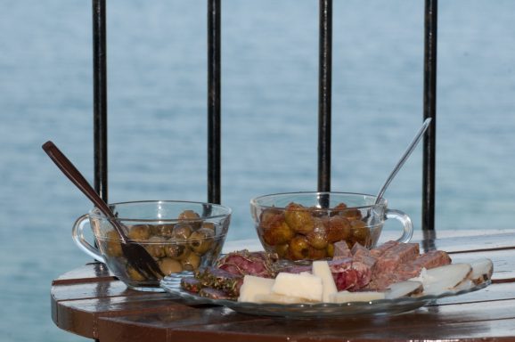 Ein Teller mit Käse, Wurst und einer Schüssel mit Marmelade am Wasser.