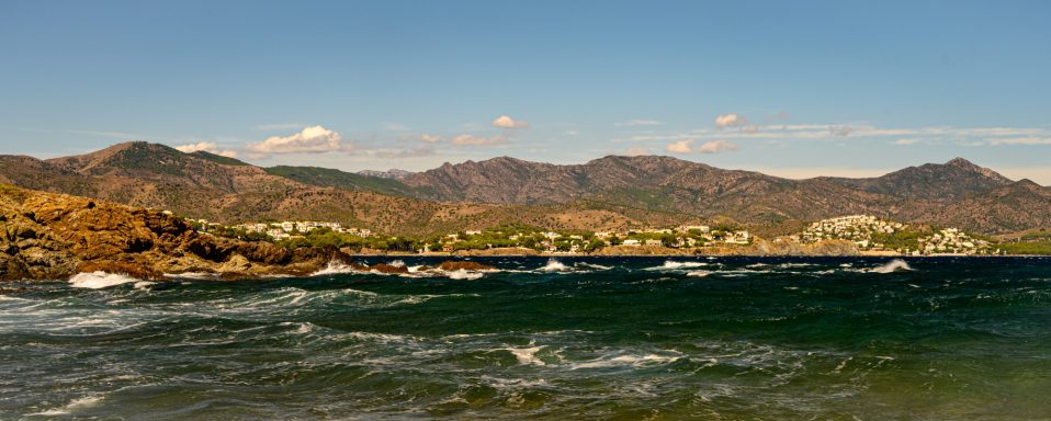 Panorama eines Küstenorts mit Bergen und Booten im Wasser.