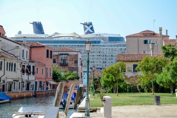 Kanalansicht mit Booten, im Hintergrund ein großes Kreuzfahrtschiff und Wohngebäude.